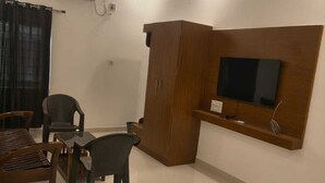 Un salon équipé d’un téléviseur, d’un meuble en bois, d’un ventilateur de plafond et de deux fauteuils.