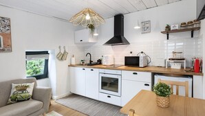 Eine moderne Küche mit weißen Schränken, einer schwarzen Dunstabzugshaube, einer Hängeleuchte und einem Essbereich mit einem Holztisch und einem Stuhl.