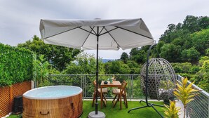 Ein Whirlpool, ein Tisch im Freien, ein Sonnenschirm und Gartenstühle auf einer Rasenfläche.