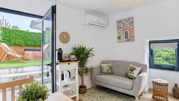 Ein gemütliches Wohnzimmer mit einer Couch, einem Couchtisch, einem Korbtisch, einer Topfpflanze und Blick ins Freie.