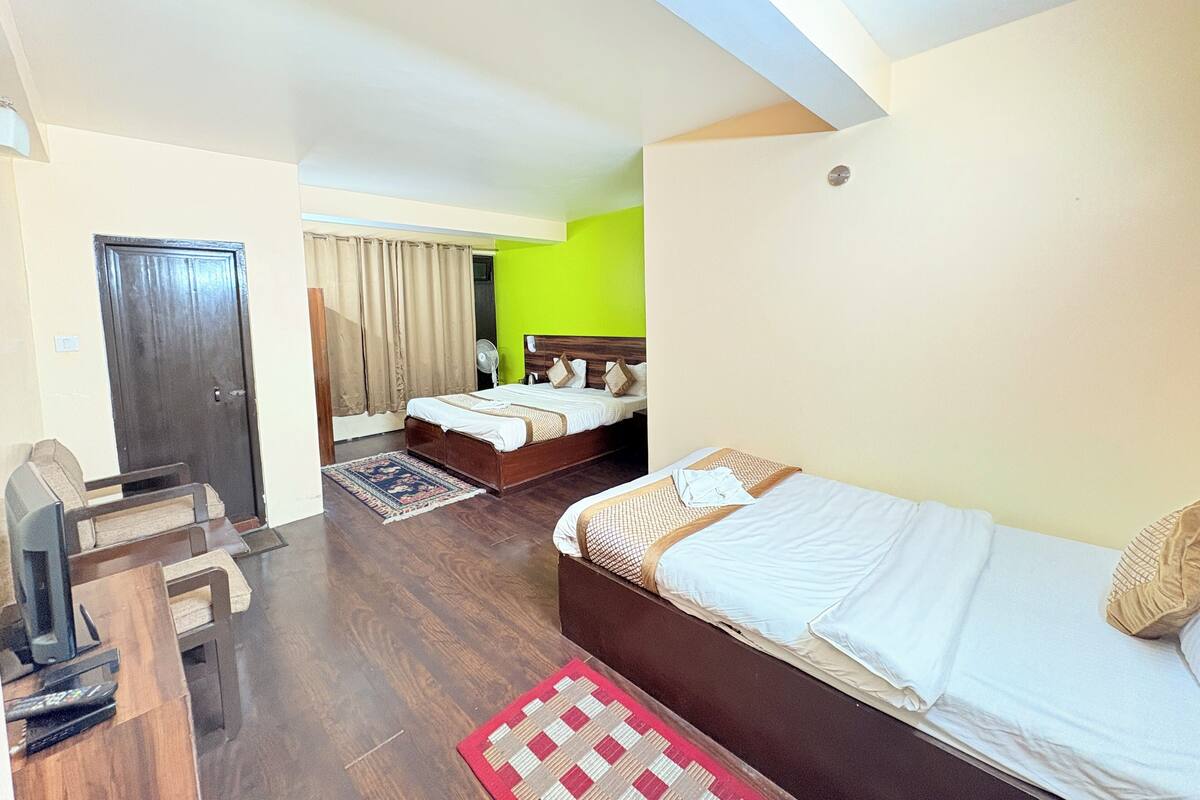 A hotel room with a wooden floor, a bed, a desk with a chair, and a television.