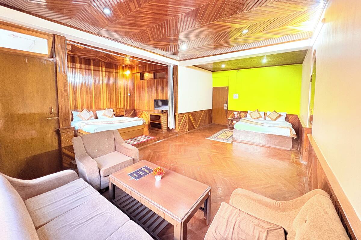 A hotel room with a wooden ceiling, two beds, a sofa, a small table, and a TV.