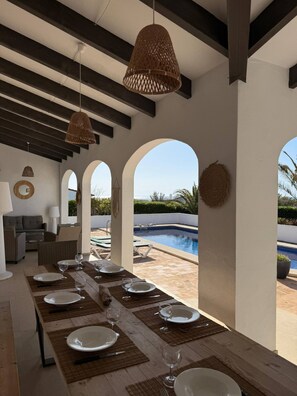 A dining area with a long table set for six, overlooking a swimming pool. - Villa for 8 with sea view and pool in S'algar (S´Algar)