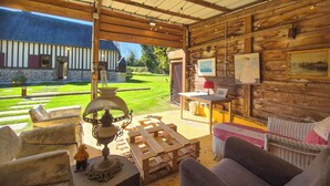 Un intérieur rustique en bois, avec une cheminée en pierre, une table à manger et une vue sur un bâtiment en pierre à l’extérieur.