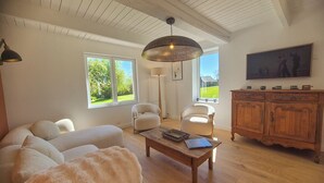 Un salon comprenant un canapé, des fauteuils, une table basse, un meuble en bois et un tableau accroché au mur.