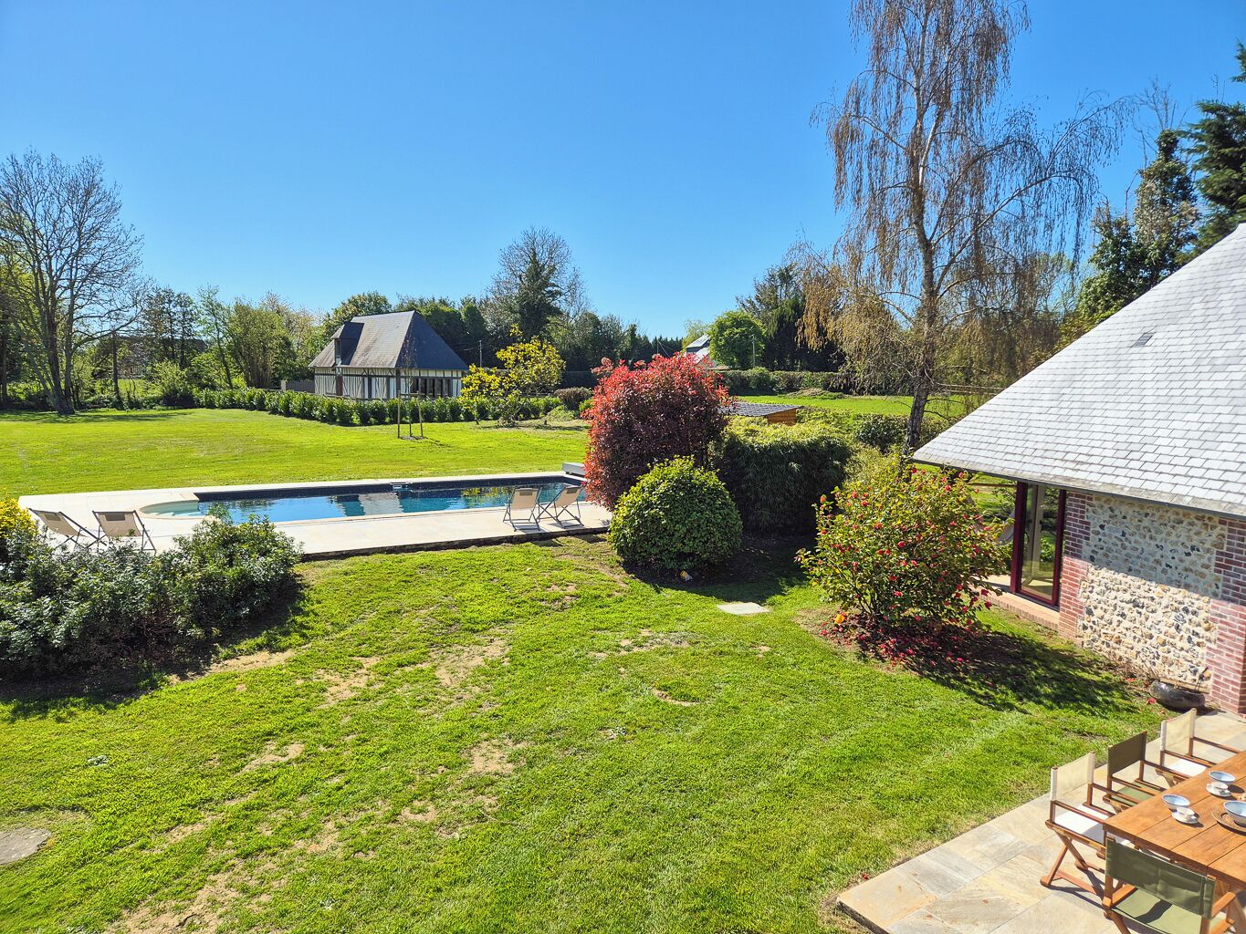 A backyard with a swimming pool, a patio table, and a brick building.