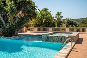 A swimming pool with a stone feature, surrounded by tropical plants and a clear sky. - Refugi Blau, sea view in Son Bou (Son Bou)