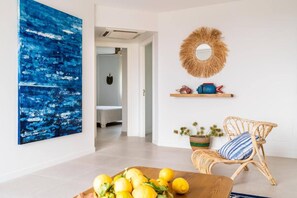 A room with a large abstract painting, a wicker chair, a wooden table with lemons, a mirror, and a shelf with decorative items. - Refugi Blau, sea view in Son Bou (Son Bou)