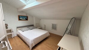 A bedroom with a bed, a desk, a chair, a radiator, and a window. - Apartment in Soulac town center, all on foot (Soulac-sur-Mer)