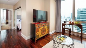Ein Hotelzimmer mit großem Fenster, einem Fernseher auf einem Schrank, einem Esstisch mit Snacks und einem Bett mit Blick.
