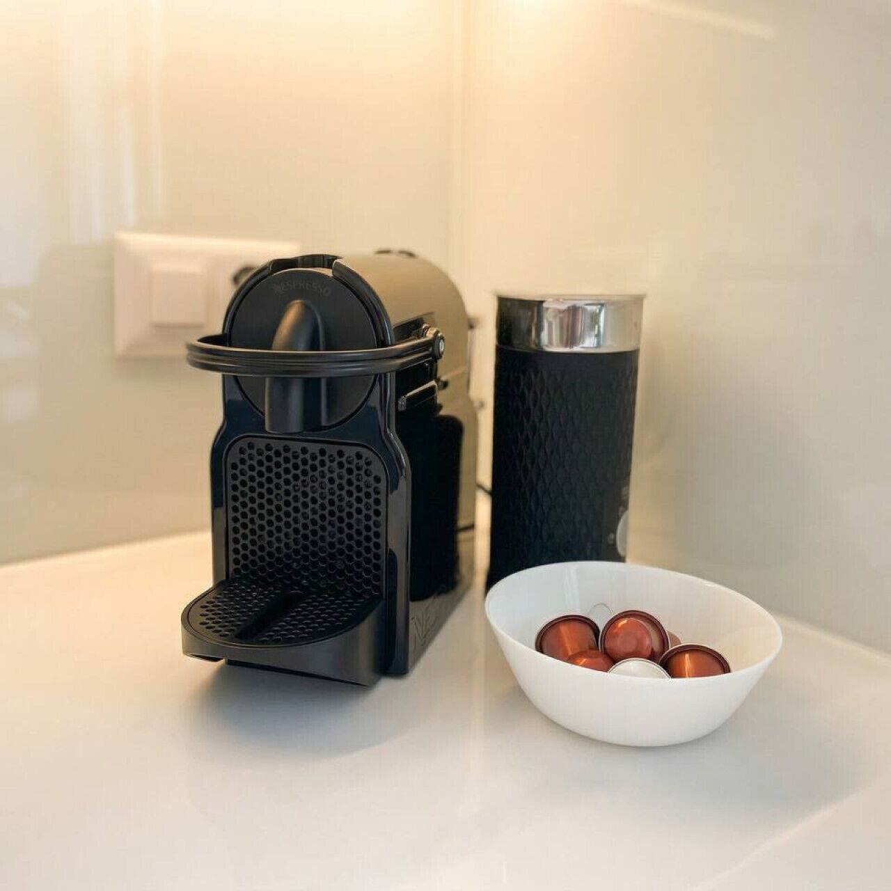 Een koffieapparaat, een prullenbak en een schaal met koffiekopjes op een aanrecht.