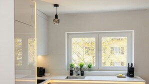 Moderni keittiö, jossa on valkoiset kaapit, sisäänrakennettu uuni, kaksi-osainen tiskiallas ja ikkuna, josta avautuu näkymä puita kohti.