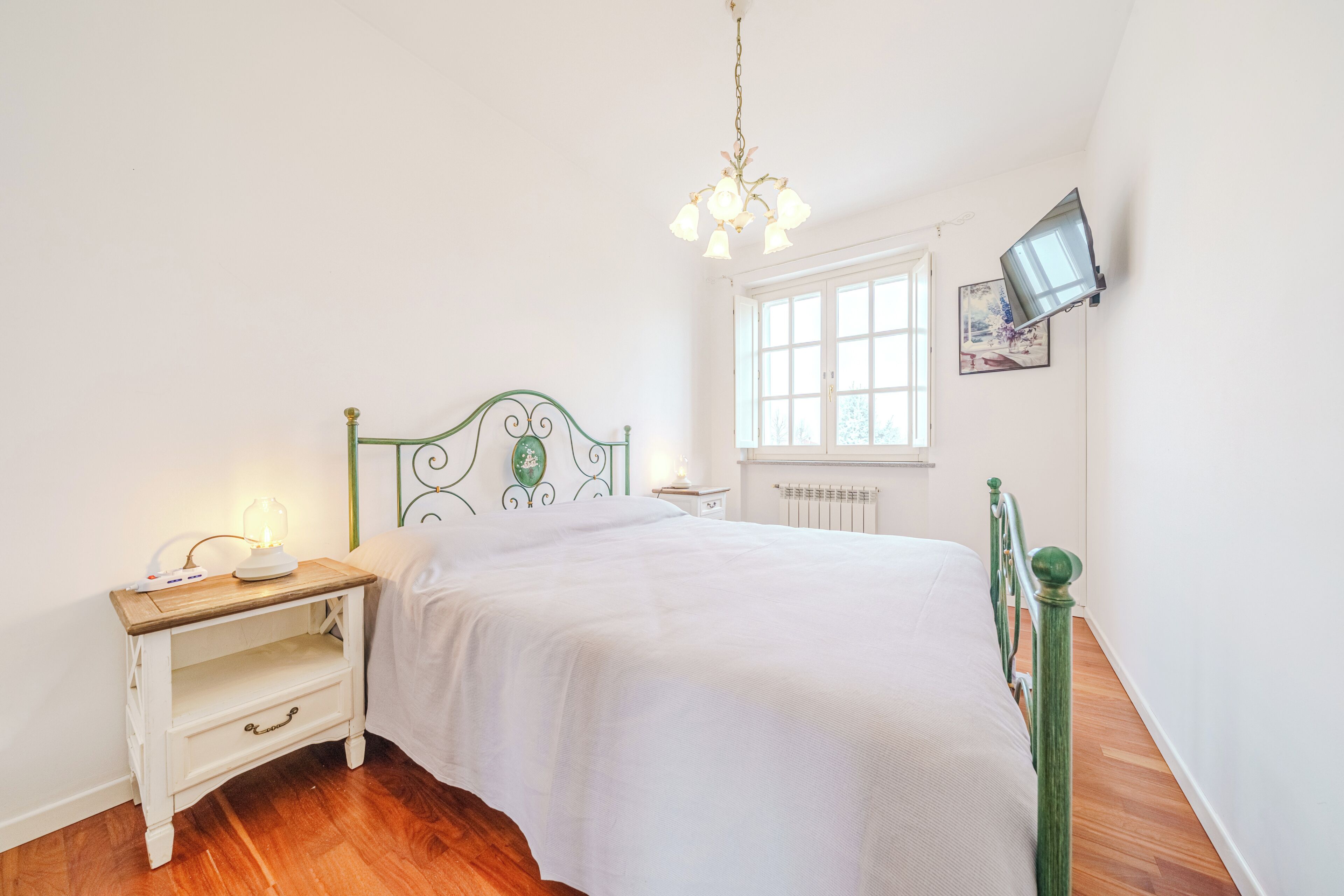 A bedroom with a bed, a nightstand, a wall-mounted TV, and a window.