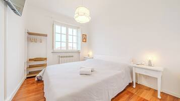 A bedroom with a bed, bedside table, nightstand, window, and a closet with hanging clothes.