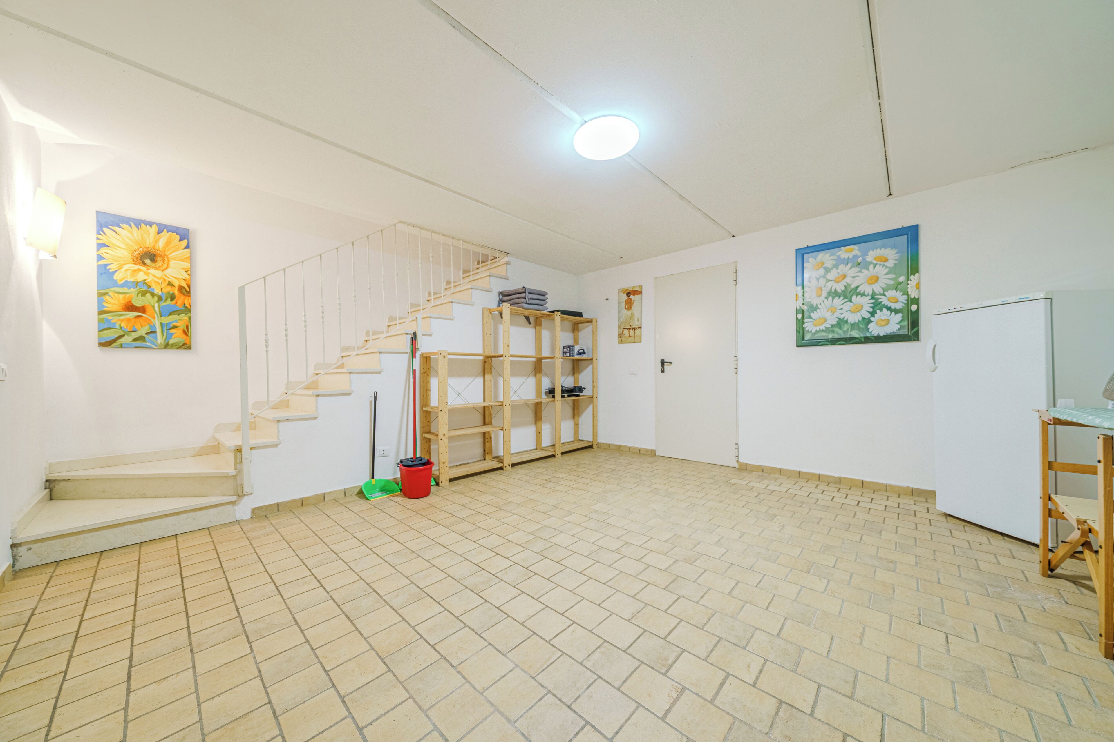 A spacious room with a tiled floor, a wooden staircase, and a door.