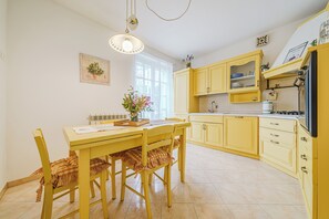 A kitchen with yellow cabinets, a dining table with chairs, a hanging light fixture, and a window with curtains.