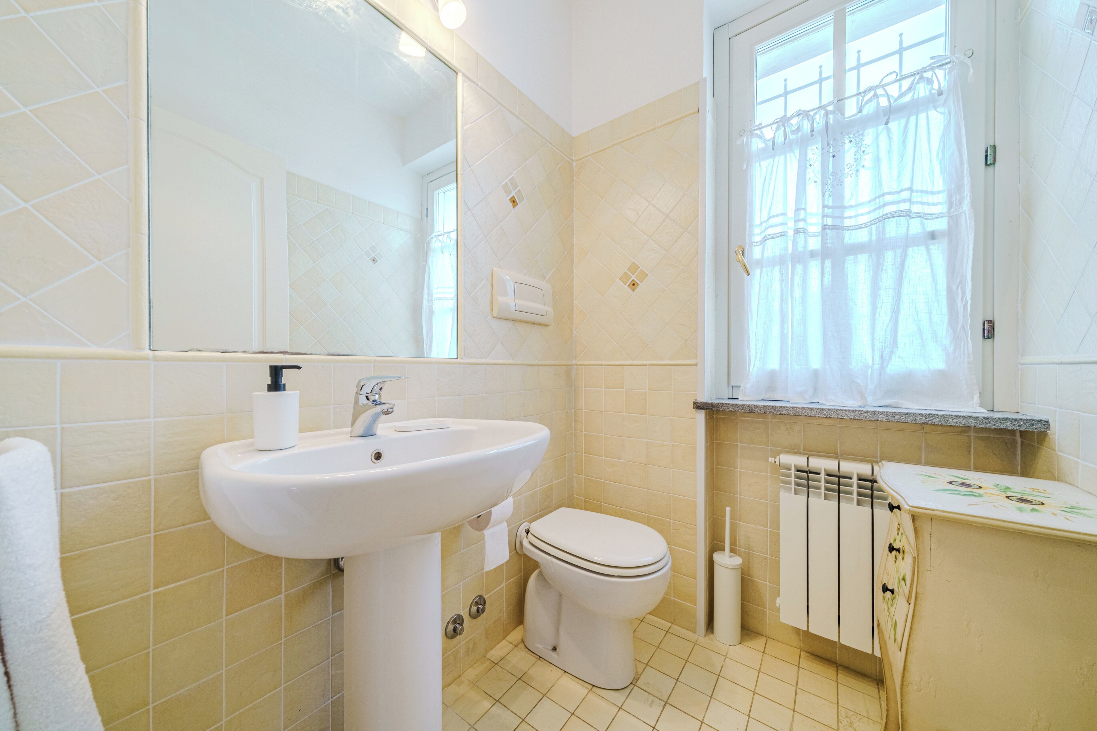 A bathroom with a sink, toilet, mirror, and window with curtains.