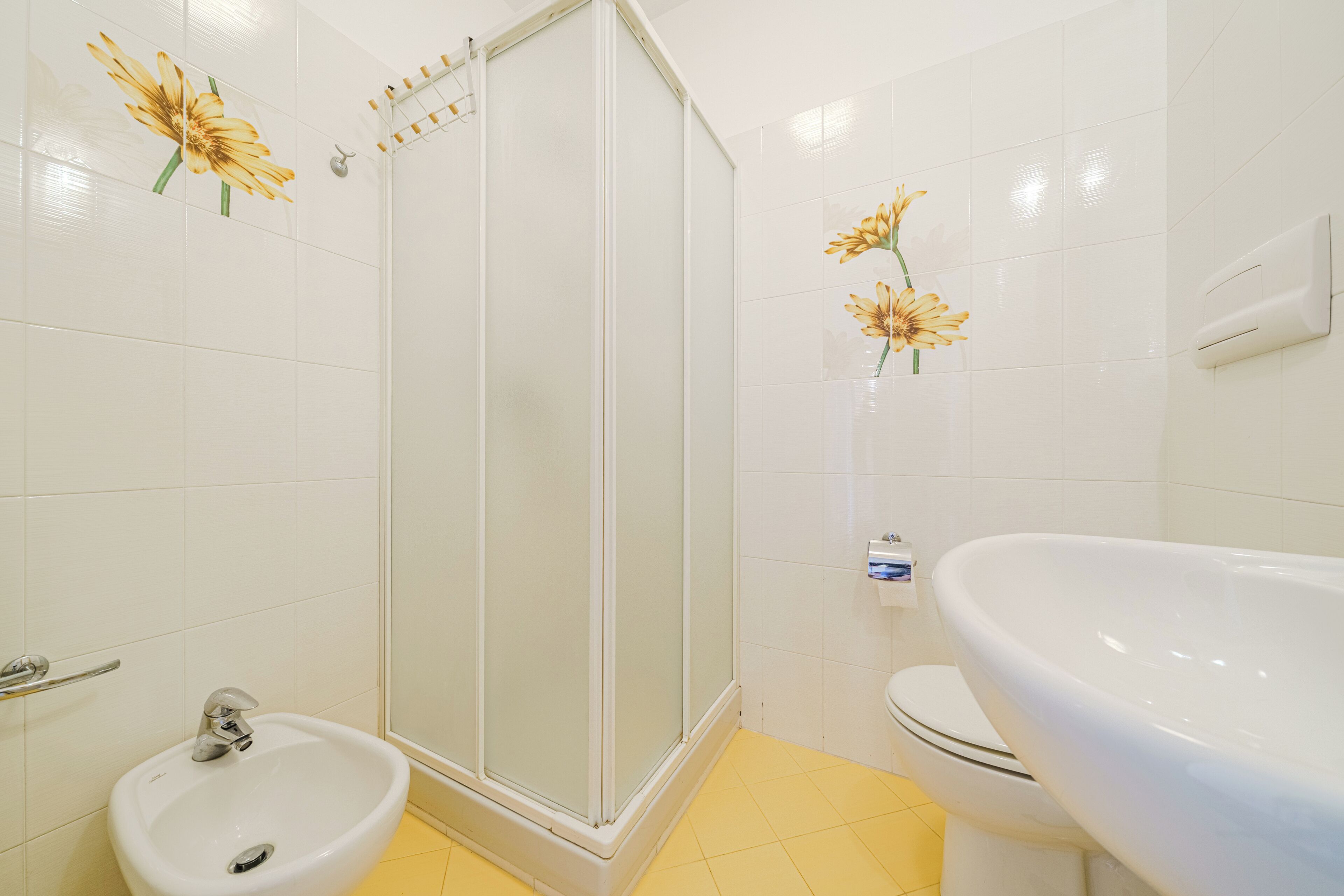A bathroom with a shower, sink, toilet, and decorative flowers.