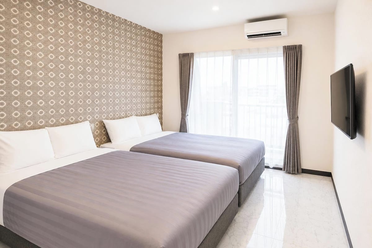 Habitación de hotel con dos camas, televisión y aire acondicionado.