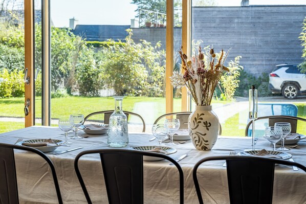 Une table à manger dressée pour quatre personnes, avec un vase de fleurs séchées, une bouteille et des assiettes.