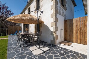 Eine Terrasse mit Tisch und Stühlen, einem Reetdachschirm, einem Holzzaun und einem Boden aus Steinplatten.