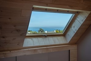 Une lucarne dans une pièce en bois, offrant une vue sur l’océan.