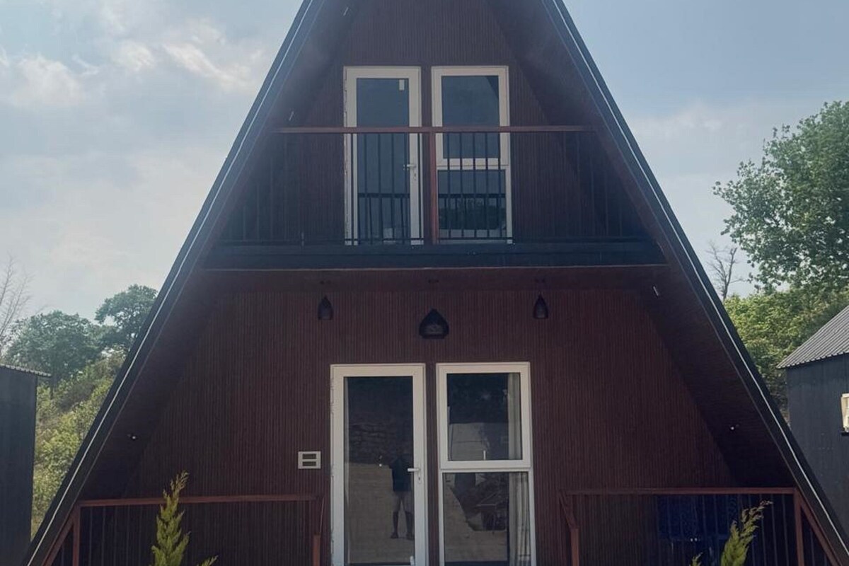 Un edificio triangular con una entrada central, dos ventanas en el piso superior y un pequeño porche.