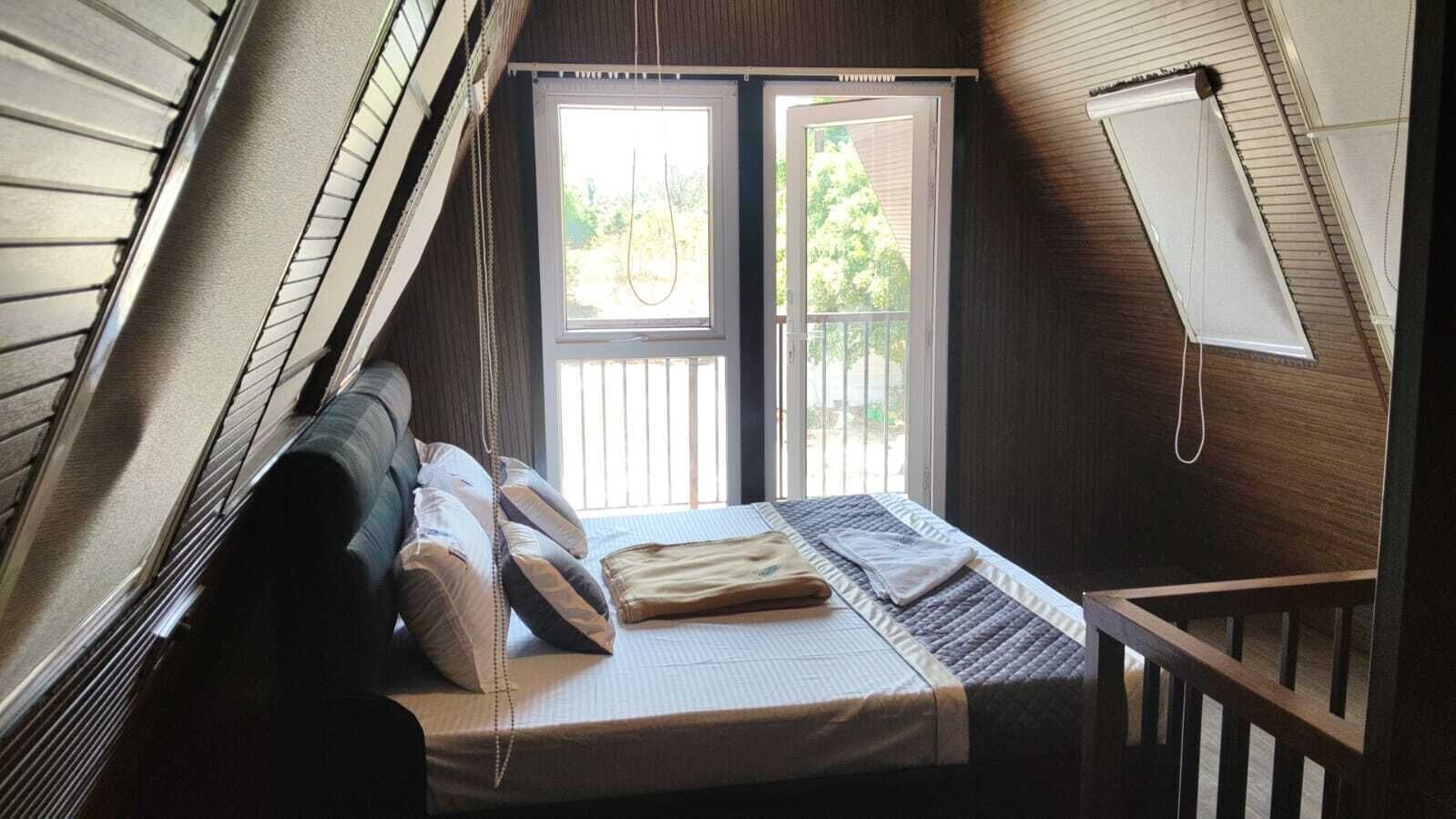 A bedroom with a bed, pillows, a blanket, a window, and a door.