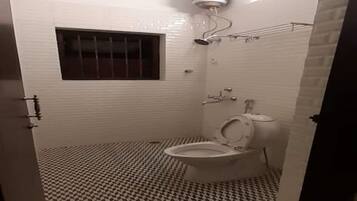 Une salle de bain avec des toilettes, une fenêtre avec des barreaux, un carrelage au sol et un chauffe-eau fixé au plafond.
