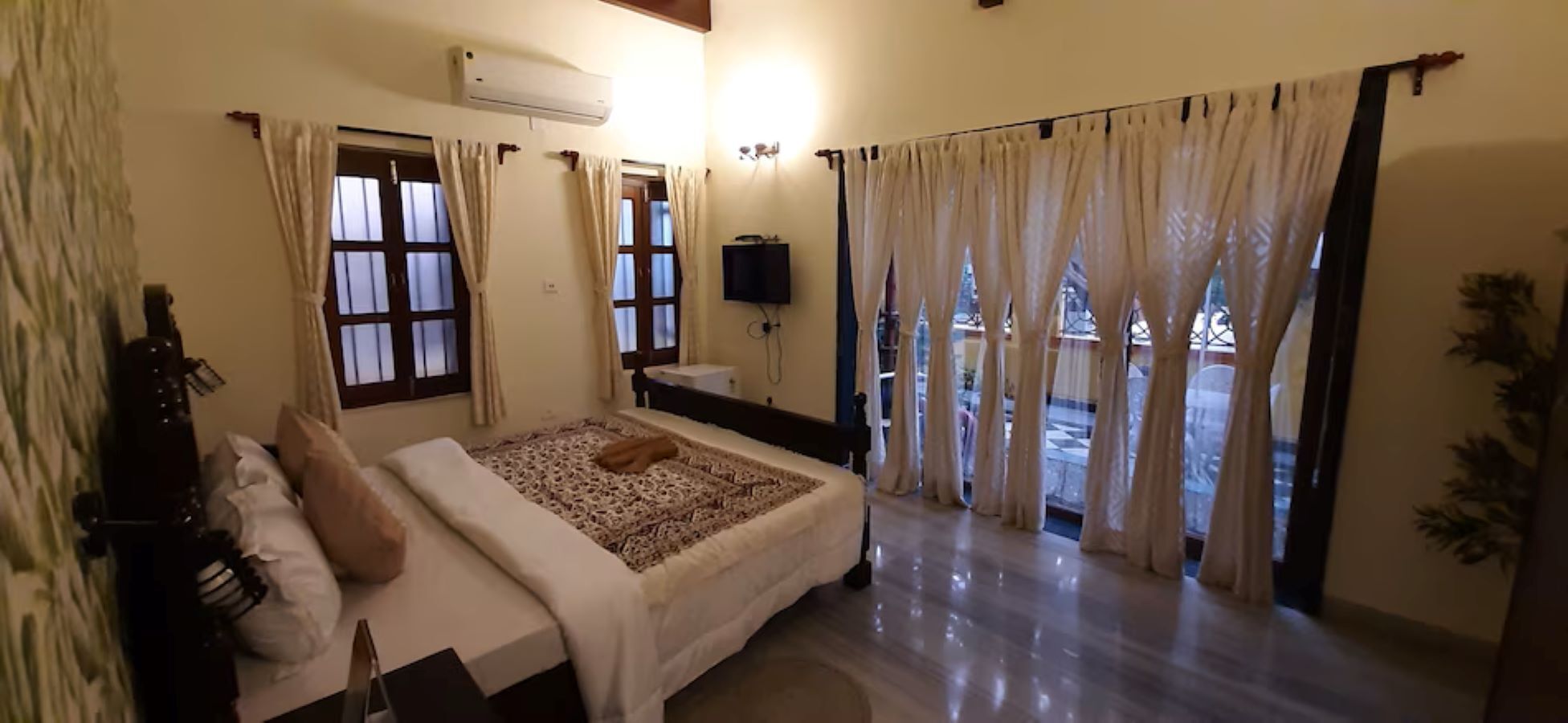 Un dormitorio con una cama, cortinas, un televisor y una ventana.