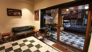 Une pièce avec un sol à carreaux, un canapé, deux fauteuils, une petite table et une porte vitrée donnant sur l’extérieur.