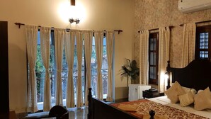 Une chambre à coucher avec un grand lit, des rideaux, une table de chevet, une lampe et une plante en pot.