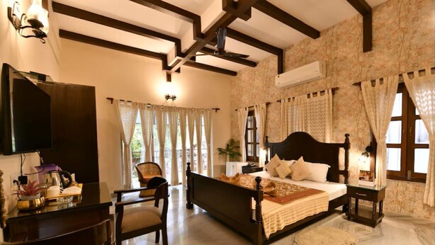 Une chambre à coucher avec un grand lit, une télévision, un bureau avec une chaise et une fenêtre avec des rideaux.