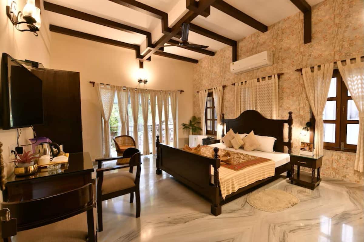 Un dormitorio con una cama grande, televisión, escritorio con silla y ventana con cortinas.