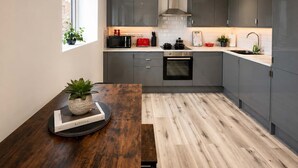 A modern kitchen with grey cabinets, a built-in oven, and a window with a plant. - The Studios at Taylor’s Court (Canvey Island)