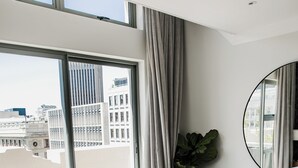 Ein modernes Schlafzimmer mit großem Fenster, rundem Spiegel und Topfpflanze.