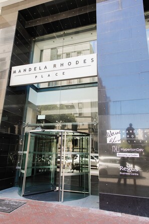 En byggnadsingång med en glasdörr och en skylt med texten ”Mandela Rhodes Place”.
