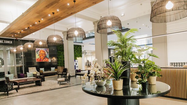 Eine moderne Lobby mit einem runden Tisch in der Mitte, verschiedenen Sitzbereichen und hängenden Pendelleuchten.