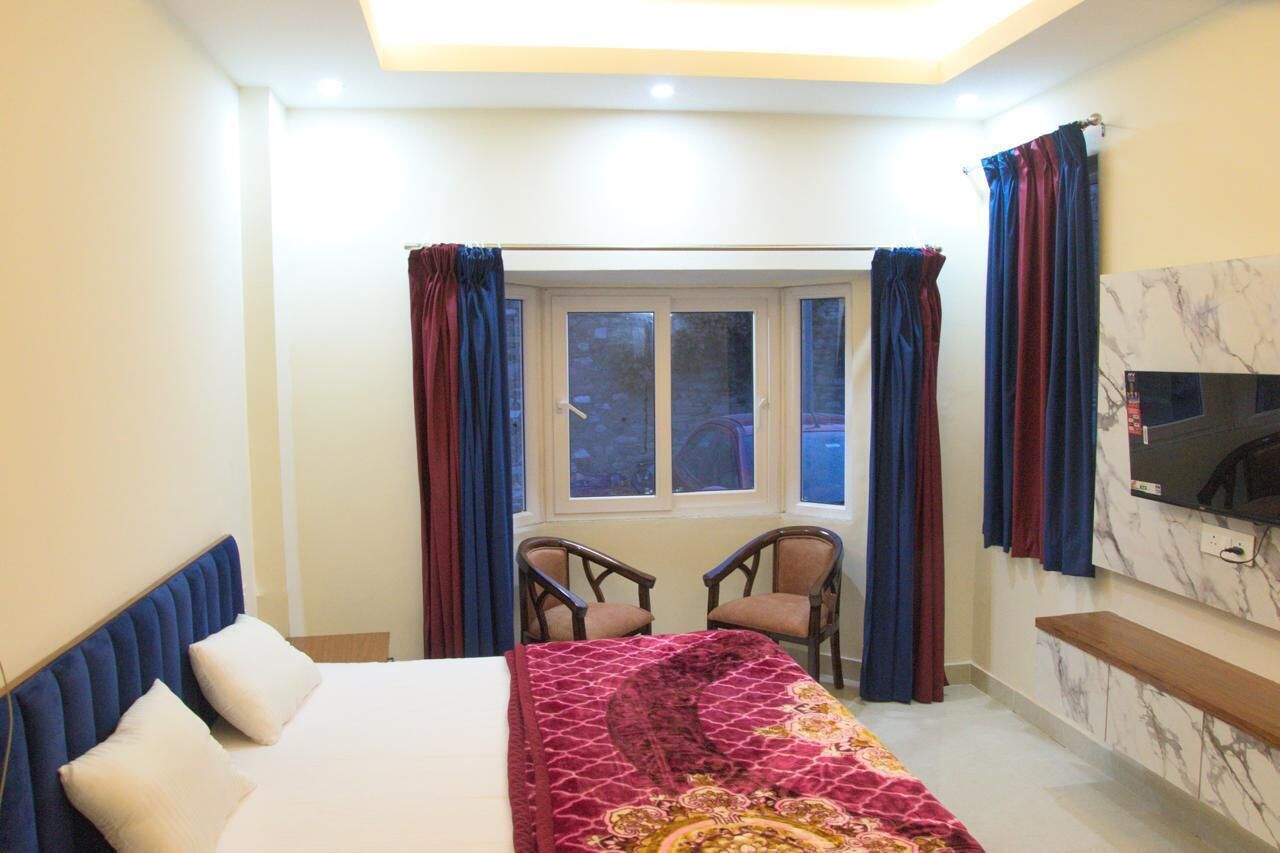 Habitación de hotel con cama, dos sillas, televisor, ventana con cortinas y pared de mármol.