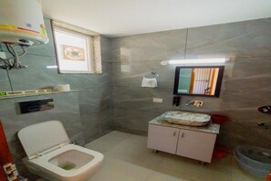 Un baño con inodoro, lavamanos con encimera de mármol, espejo y barra para toallas.