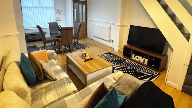 Ein Wohnzimmer mit einer Couch, einem Couchtisch und einer TV-Konsole. Eine Treppe befindet sich rechts.