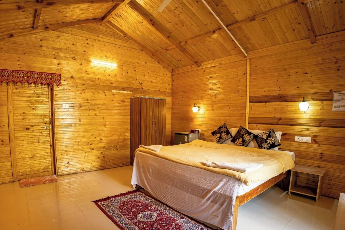A wooden cabin bedroom with a bed, a nightstand, a wall-mounted lamp, and a red patterned rug.