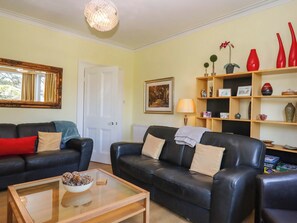 A living room with two black leather sofas, a glass coffee table, a white door, a framed painting, and a bookshelf with various items. - Avenue Park Villa (Torquay)