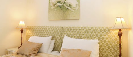 Una cama bien hecha con un cabecero estampado, dos lámparas de noche y una obra de arte floral en la pared.