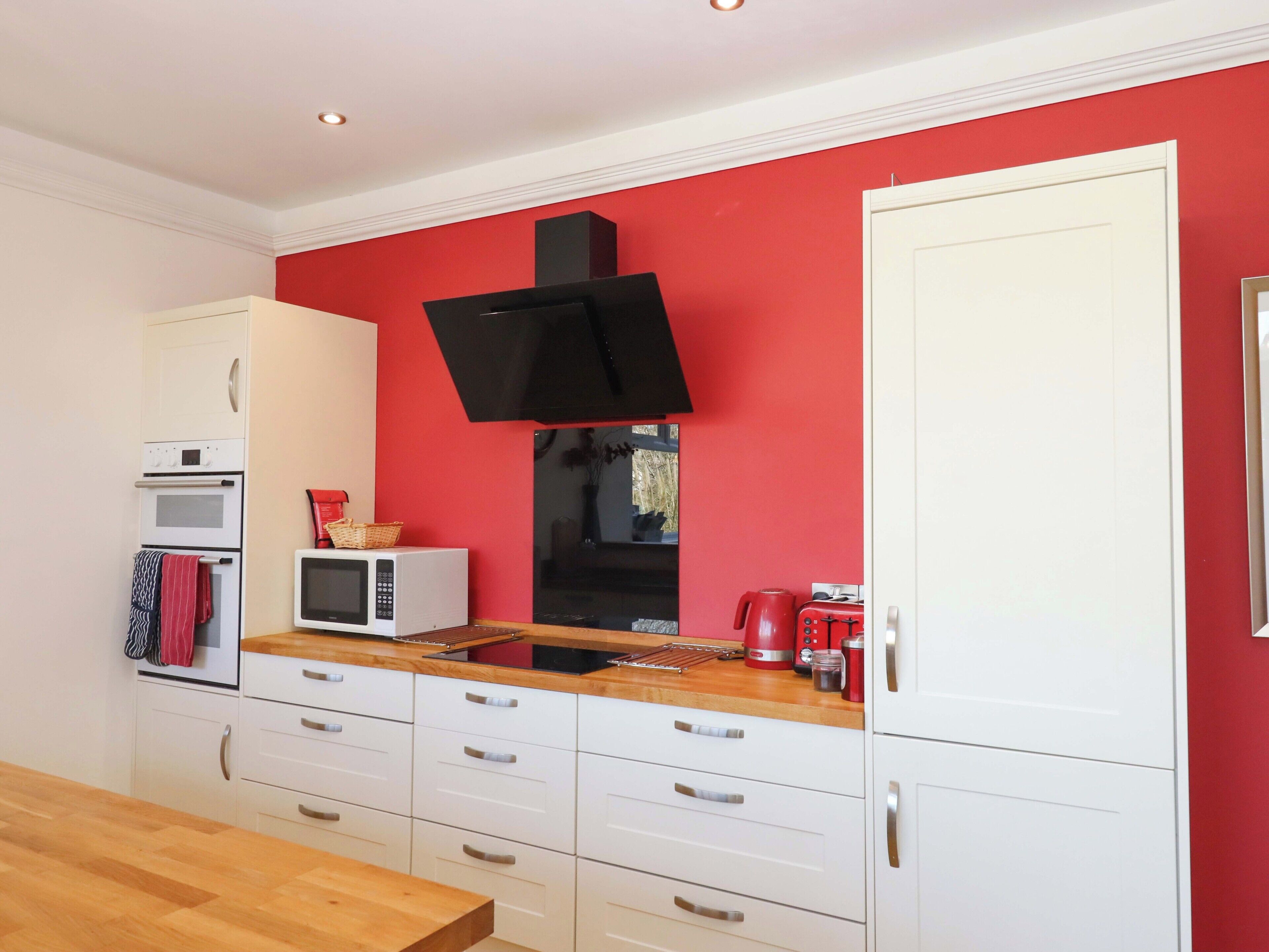 Une cuisine de taille réduite avec des meubles blancs, un four à micro-ondes, un grille-pain et un mur rouge.