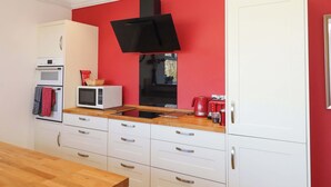 A compact kitchen with white cabinets, a microwave, a toaster, and a red wall. - Avenue Park Villa (Torquay)