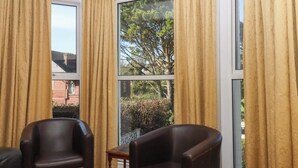 A room with two leather chairs, a small table, and large windows with curtains. - Avenue Park Villa (Torquay)