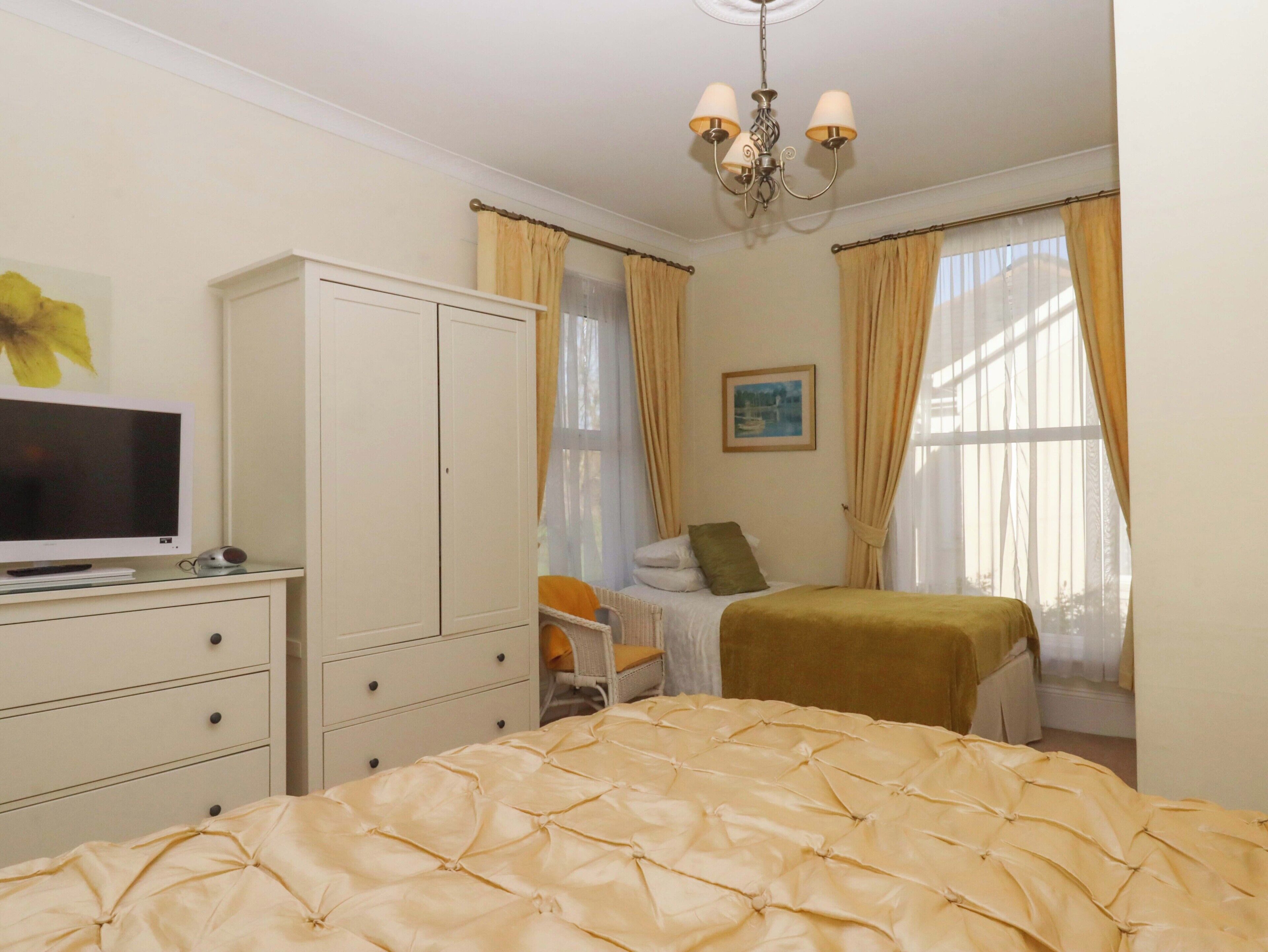 A bedroom with a bed, a TV on a dresser, a wardrobe, and a painting on the wall.