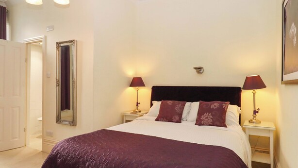 A bed with a dark headboard, two bedside lamps, and a large mirror on the wall. - Avenue Park Villa (Torquay)