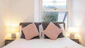 Uma cama bem arrumada com travesseiros, uma janela com vista e abajures.